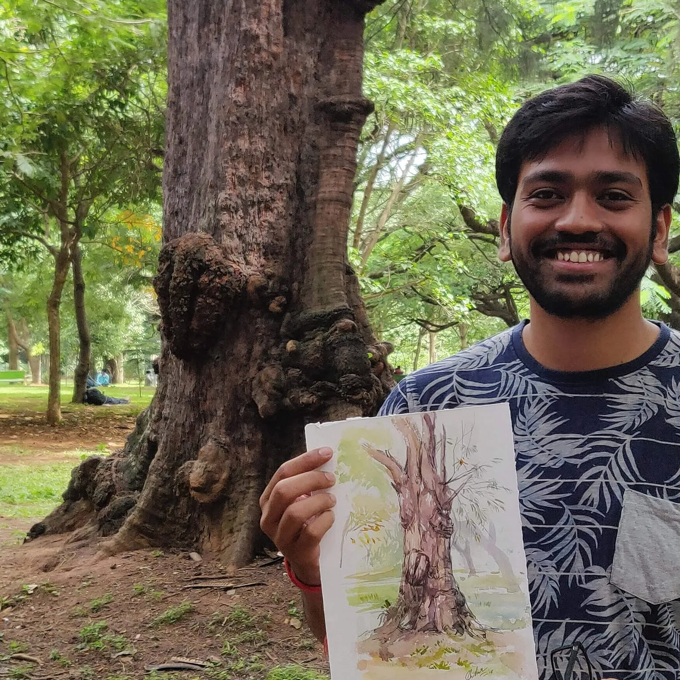 Shishir holding a watercolour sketch beside the tree he painted